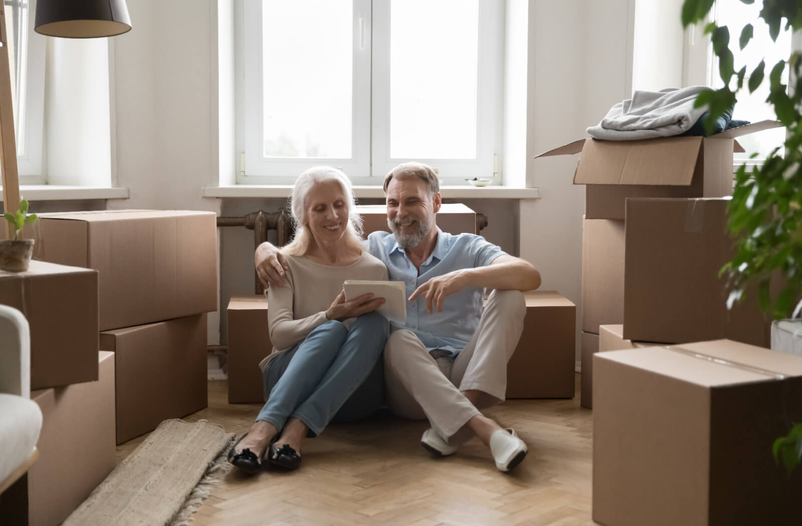 An older married couple sitting on the floor of their packed-up home reviewing their checklist for a move to assisted living.