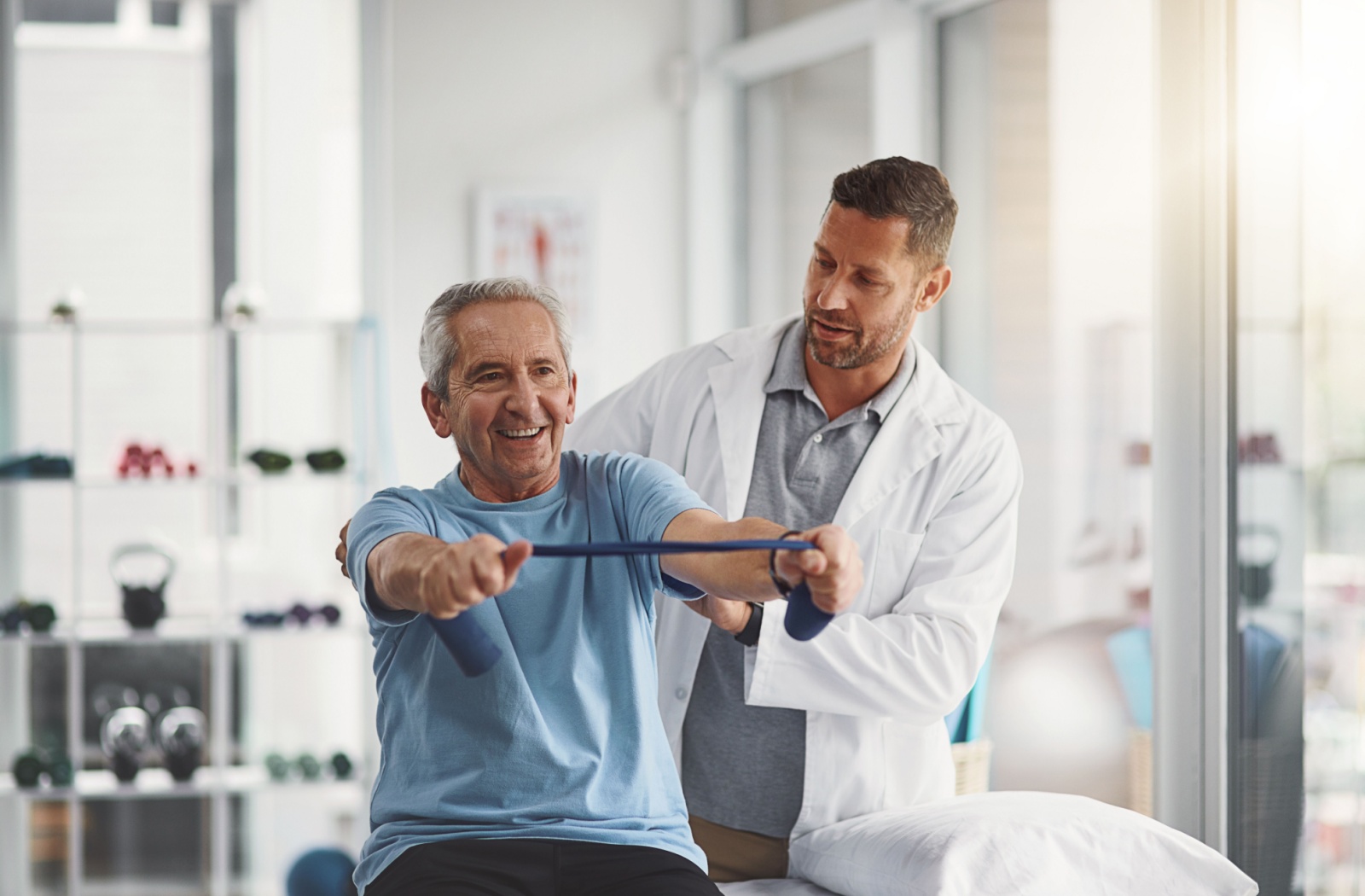 An older adult doing seated resistance-band training with the help of a physiotherapist.