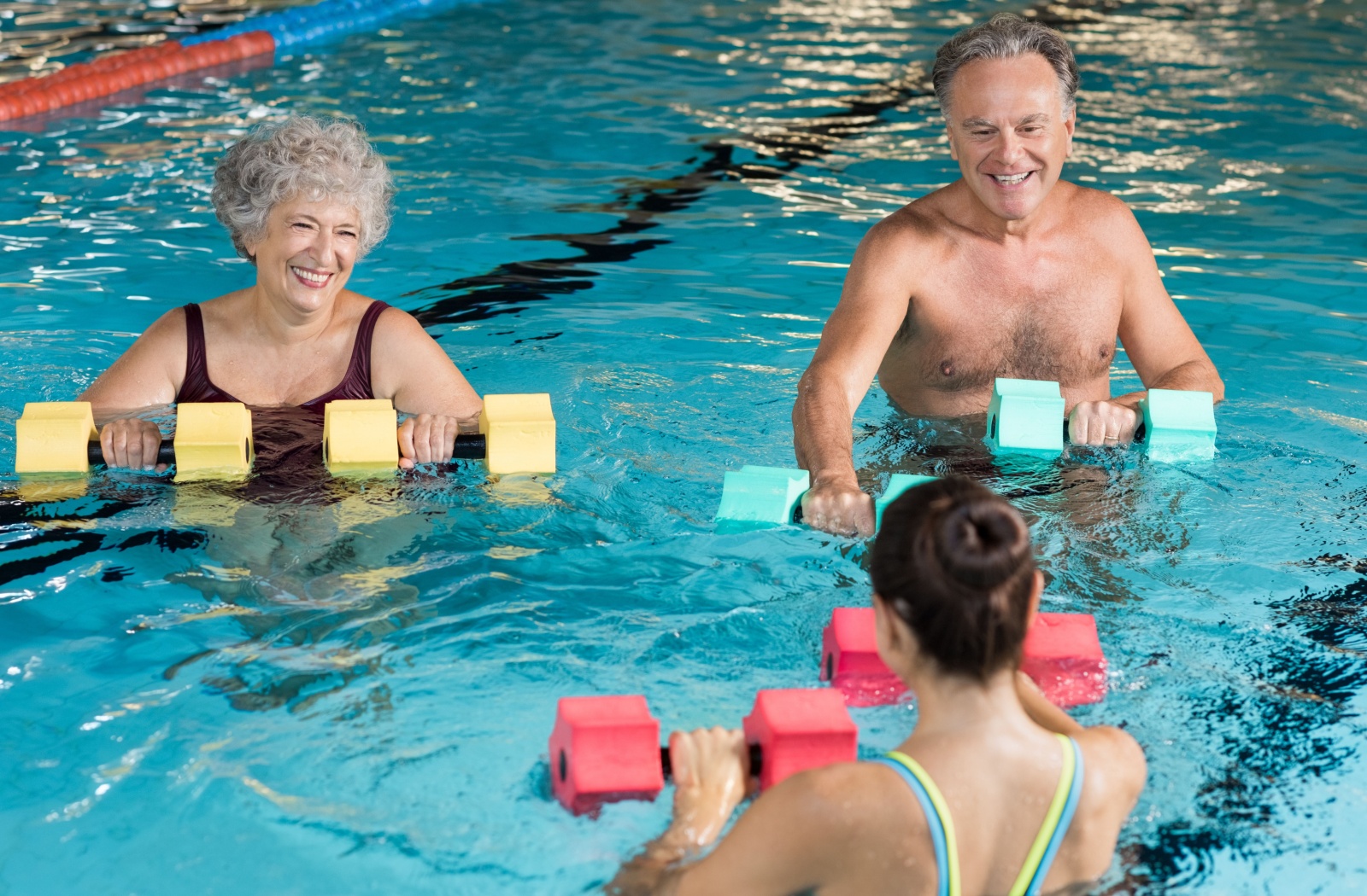 2 older adults doing weight exercises with an instructor in water aerobics.