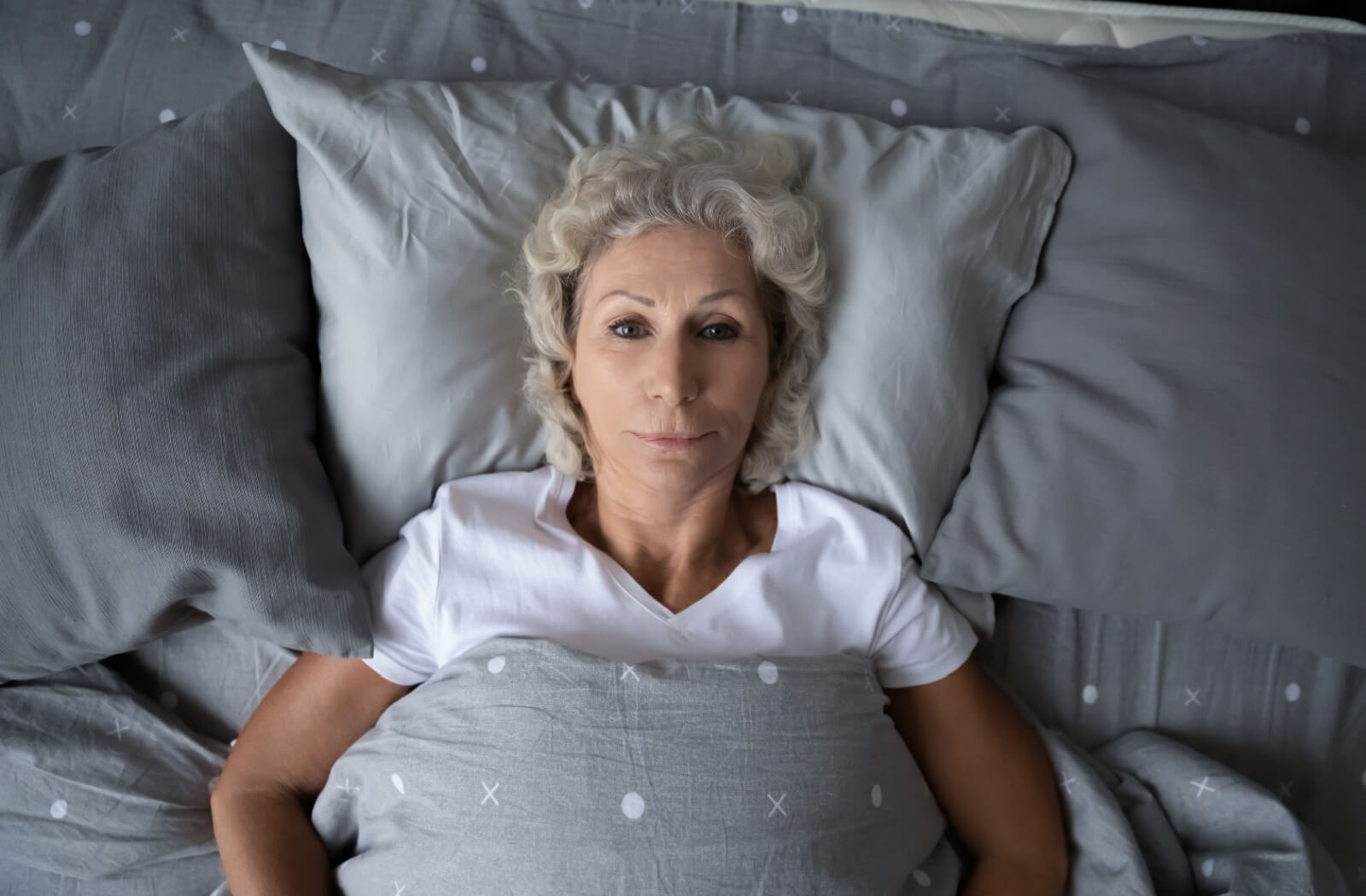 An overhead image of an older adult with dementia lying awake at night on grey bedding.