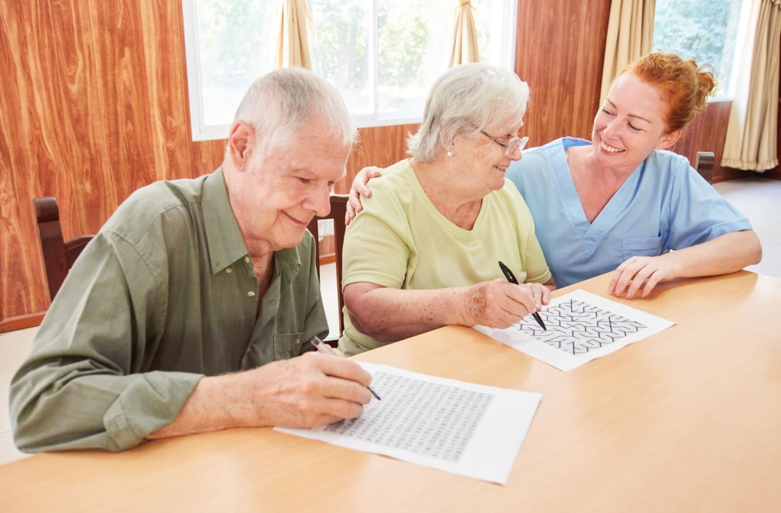 An older adult couple solving a puzzle while being monitored by a memory care staff