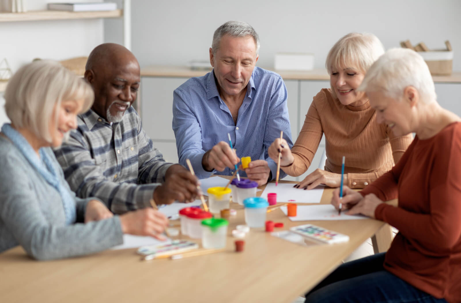 A group of older adults in assisted living laughing around a table during an arts and crafts hobby class.