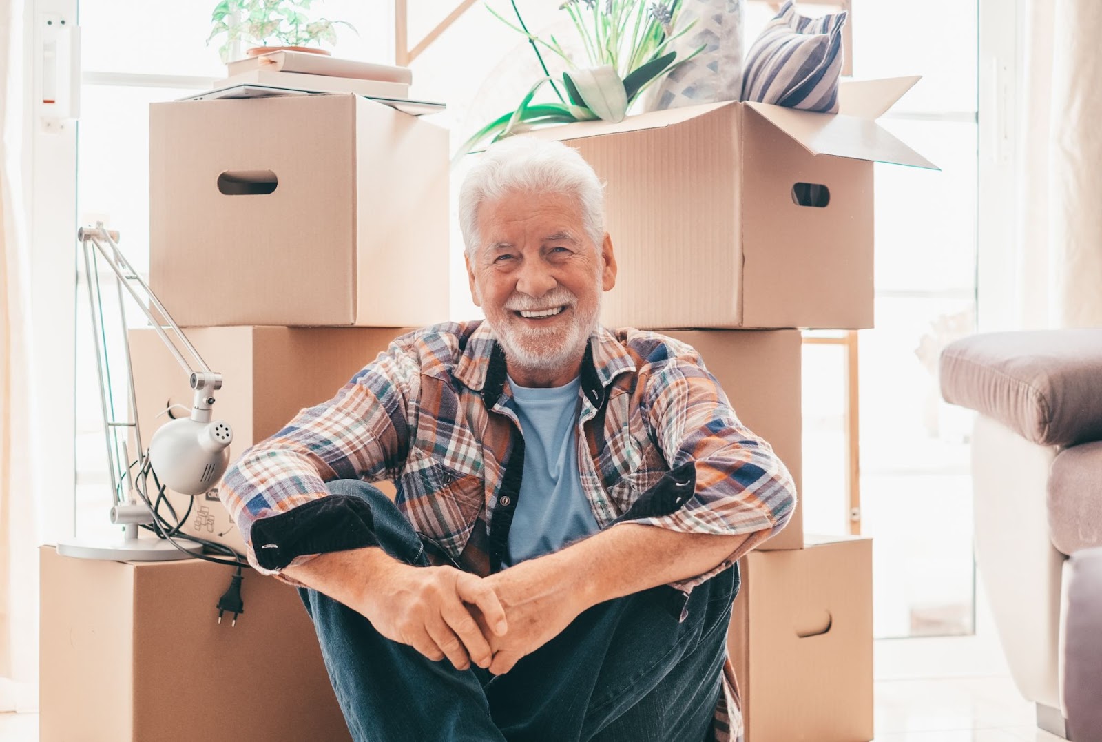 A smiling older man sitting in front of several full moving boxes.