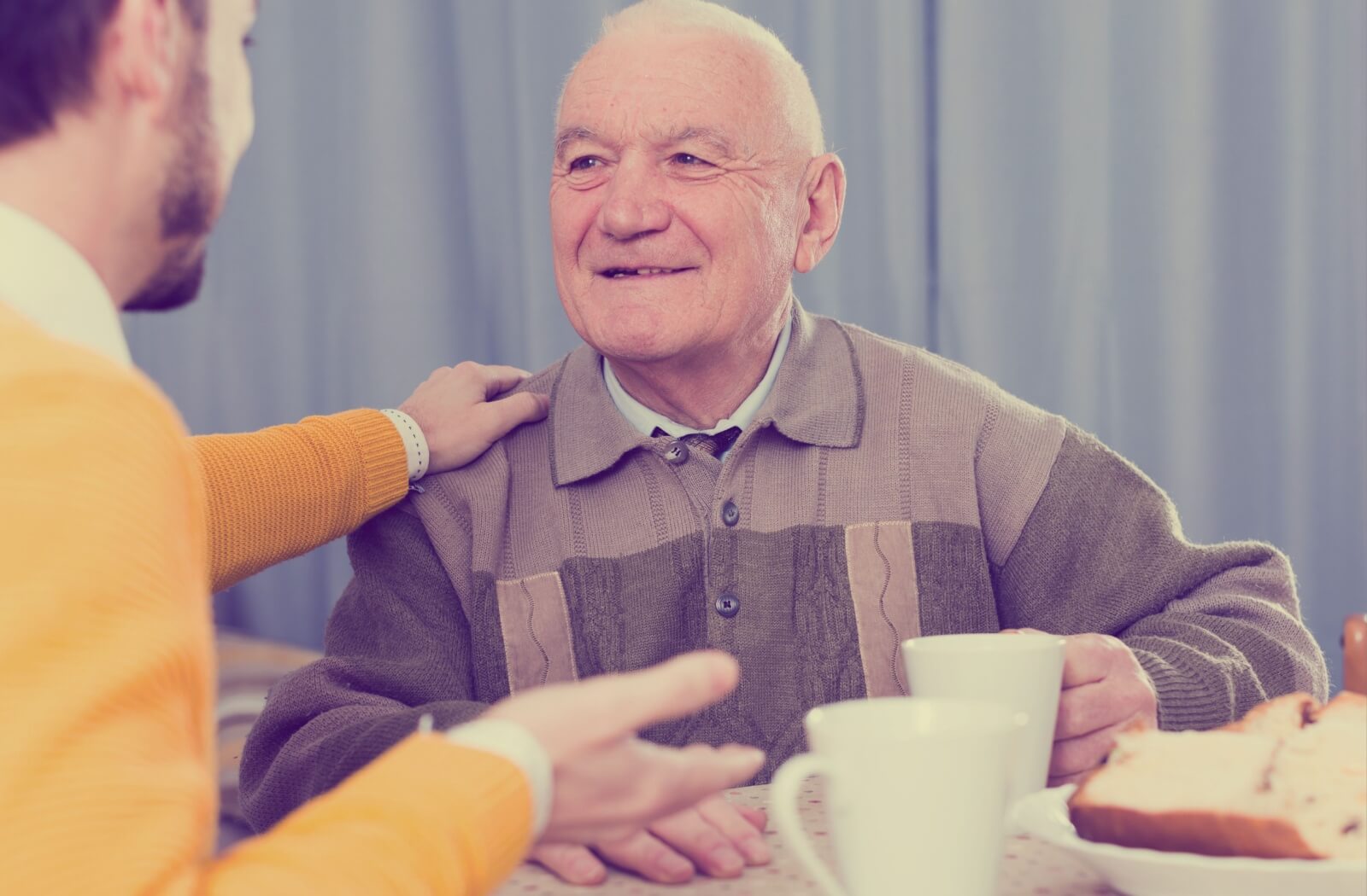 A smiling senior enjoys a nice chat with their adult child while they share a meal.