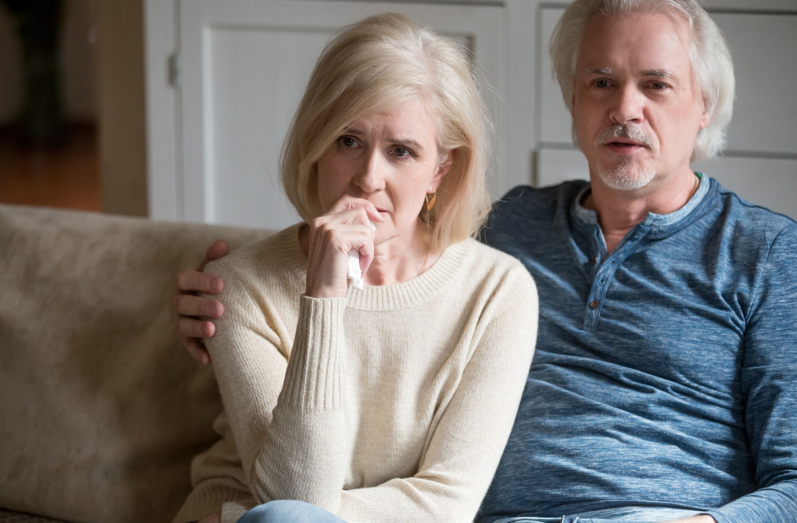 A concerned older adult and their spouse watch a serious movie about Alzheimer's disease on their couch at home
