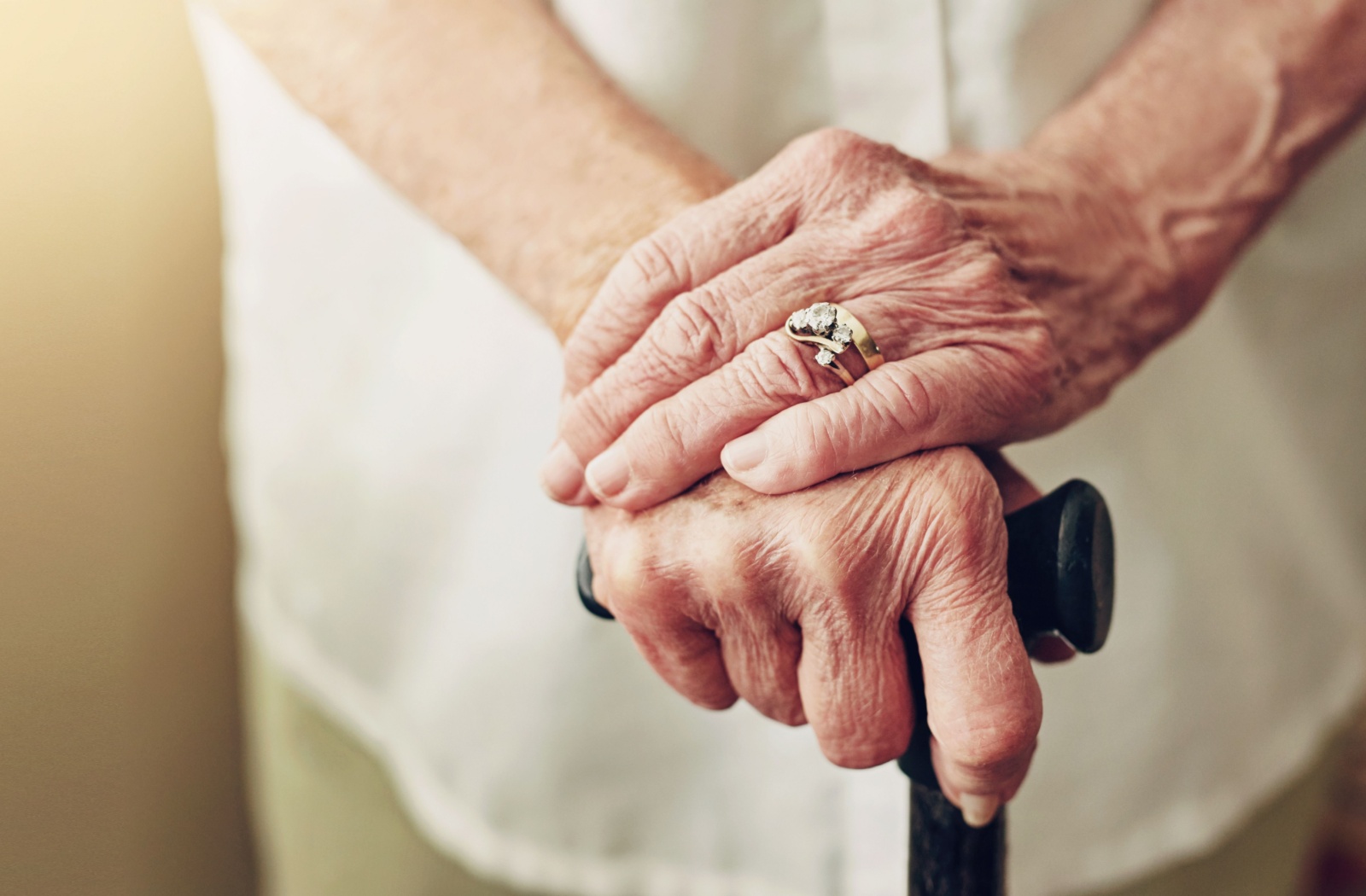 A close-up image of an older adult resting their hands atop their cane to help with their balance