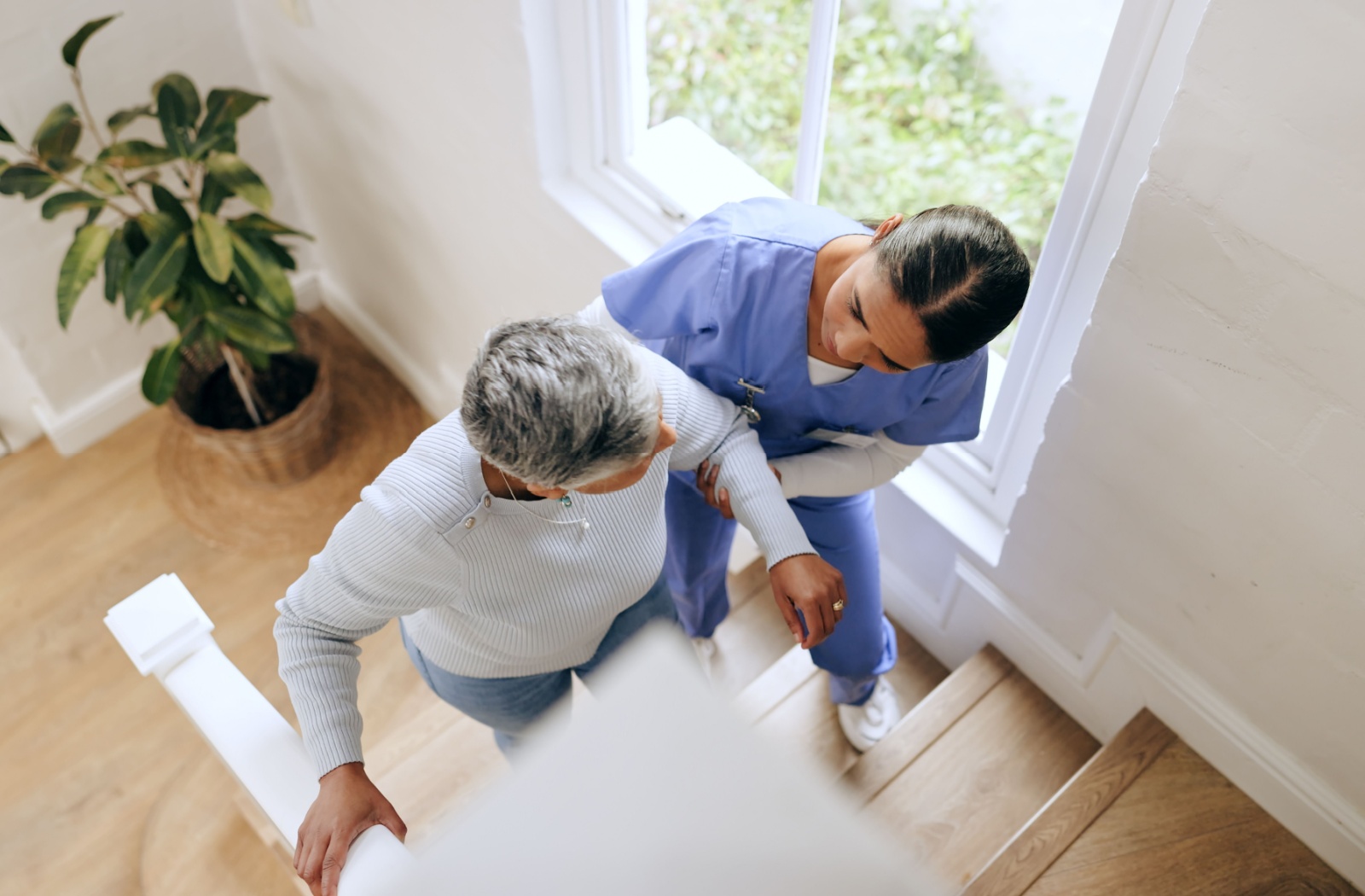 A caregiver carefully helps an older adult walk up the steps of their well-lit apartment in assisted living